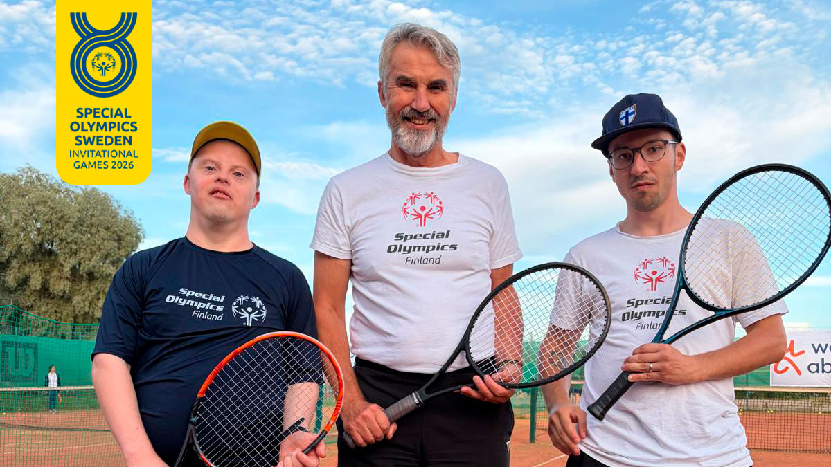 Suomen joukkueen tennispelaajat ja valmentaja poseeraamassa kameralle iloisena mailat kädessä kentällä.